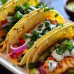 A platter of vibrant fish tacos with grilled fish, fresh veggies, creamy sauce, and cilantro, served on warm tortillas.